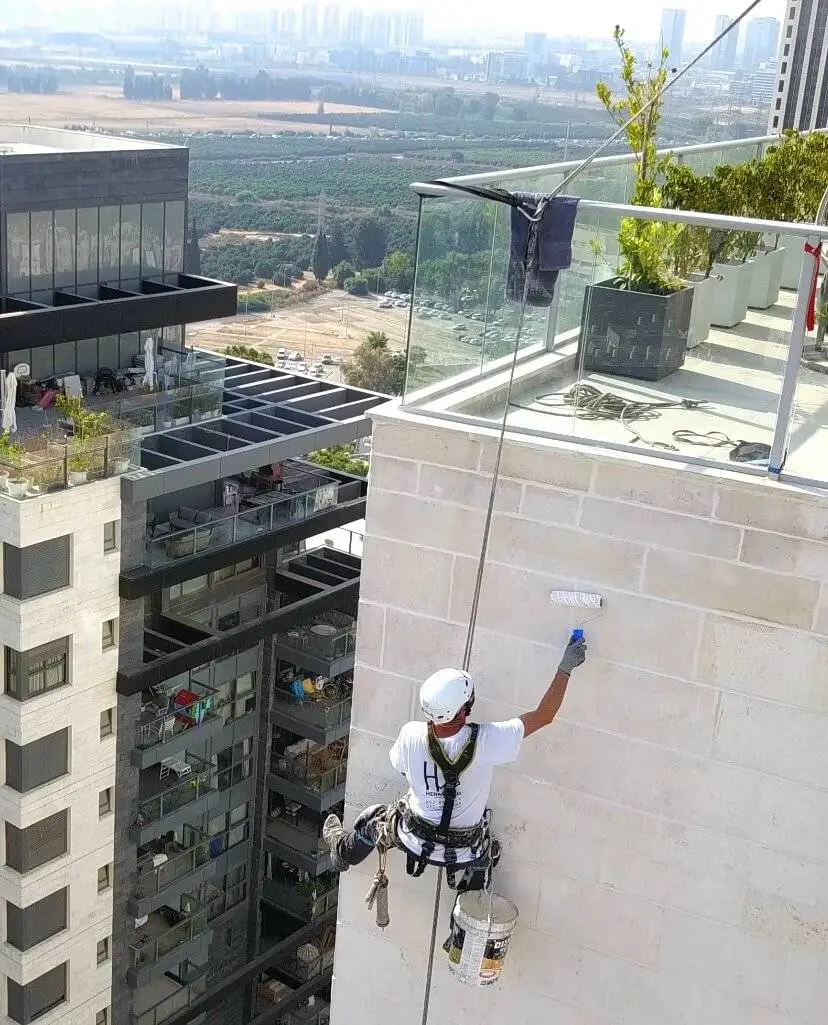 שני עובדי הרמטיקו רתומים לחבלים ומבצעים עבודת איטום על קיר חיצוני של בניין רב-קומות