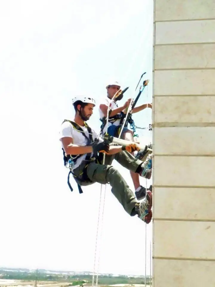 עובד הרמטיקו בסנפלינג על חזית אבן של מגדל מול שמיים כחולים